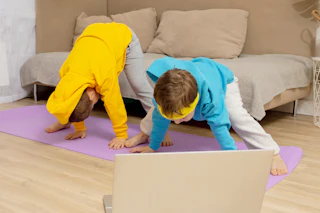 Two little caucasian kids doing fitness exercises at home. Children have fun during sport. Boys make training, looking at computer. Sport, yoga online. Workout in the apartment. Healthy lifestyle